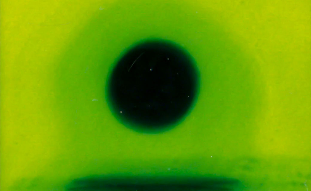 a detail from Kei Ito's "New Light -- Narrowcast," in which he turns films of nuclear testing into still photographs and then back into a film; this detail of a shot shows a black circle on a green background