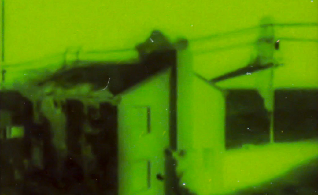 a detail from Kei Ito's "New Light -- Narrowcast," in which he turns films of nuclear testing into still photographs and then back into a film; this detail of a shot shows a house and power lines in green and black