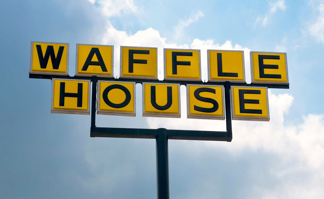 A photograph of a Waffle House sign (with black letters, each on a yellow rectangle) against a blue sky with white clouds